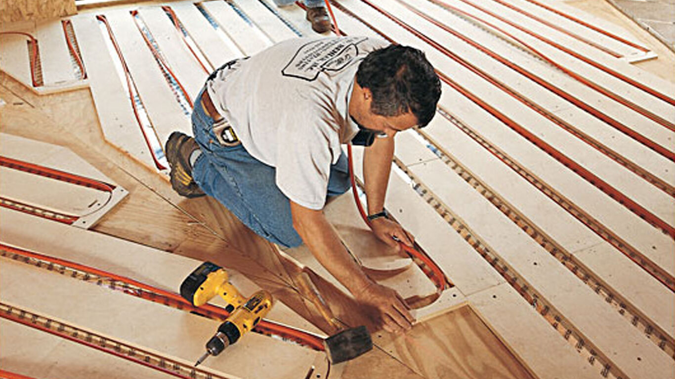 Man on his knees installing heating flooring.