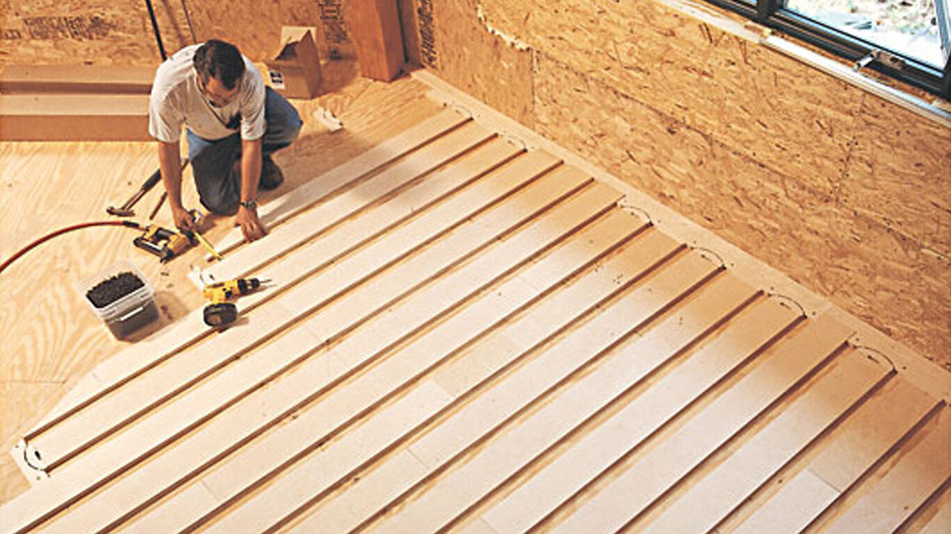 Man on his knees installing heating flooring.