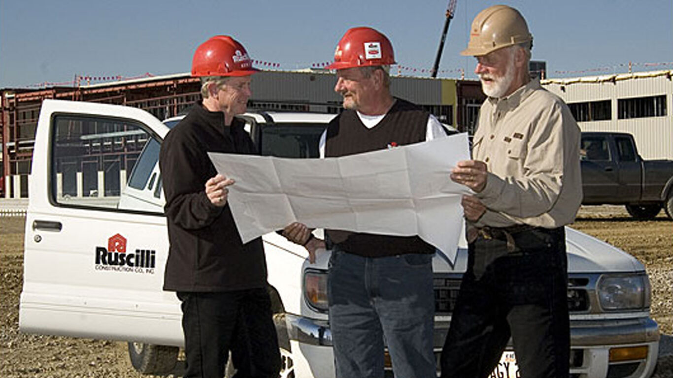 Three men all looking at building plan on a construction site, standing in front of a white truck